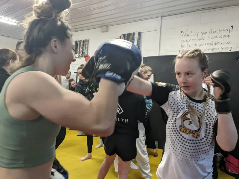 A young woman throwing a punch at pads held by a female coach